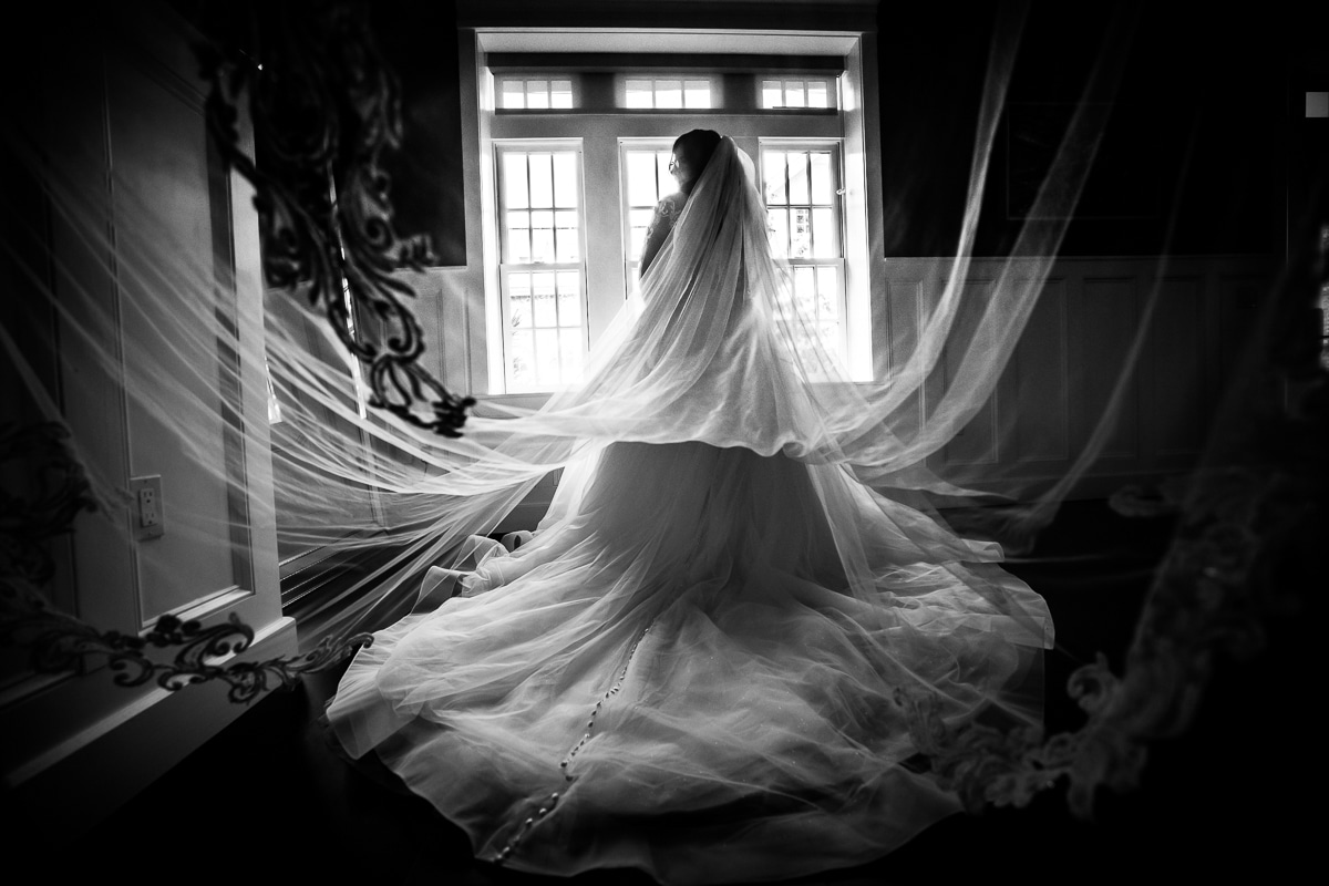 Ryland Inn Wedding Photographer, lisa rhinehart, captures a black and white image of the bride standing in front of the window in her dress with her veil draped out in several directions during her preparation pictures before her wedding ceremony 
