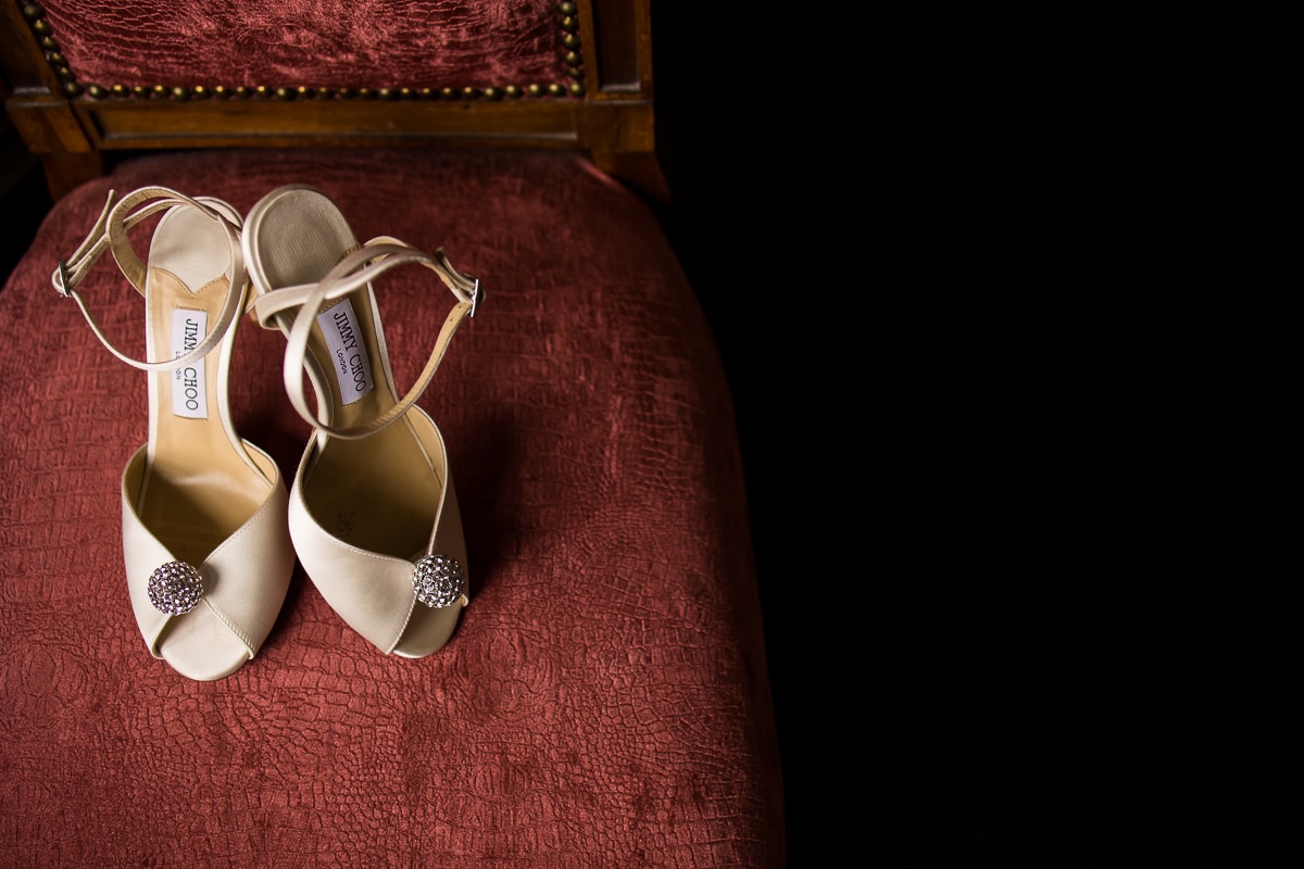 Detail photo of the brides jimmy choo shoes sitting on a red velvet chair during the preparations before the wedding 