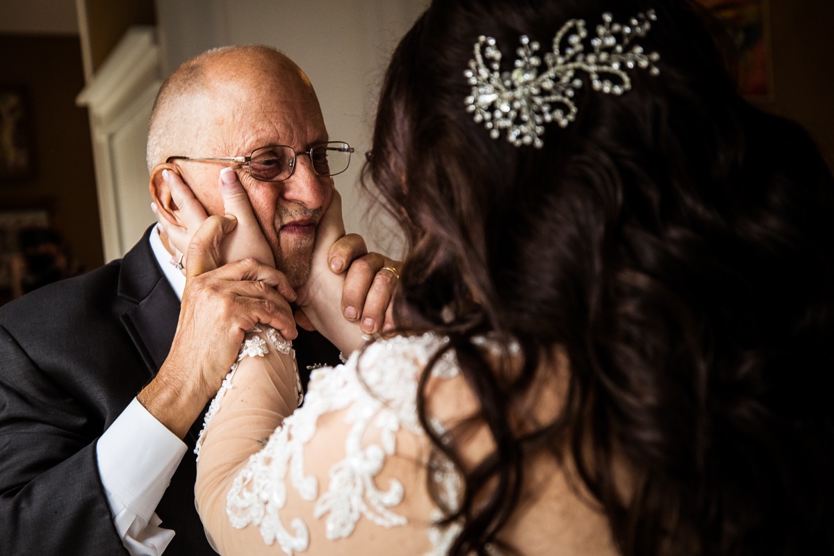 image of the bride holding her dads face as he holds her hands and he looks at her during their parent first look at the Ryland Inn 