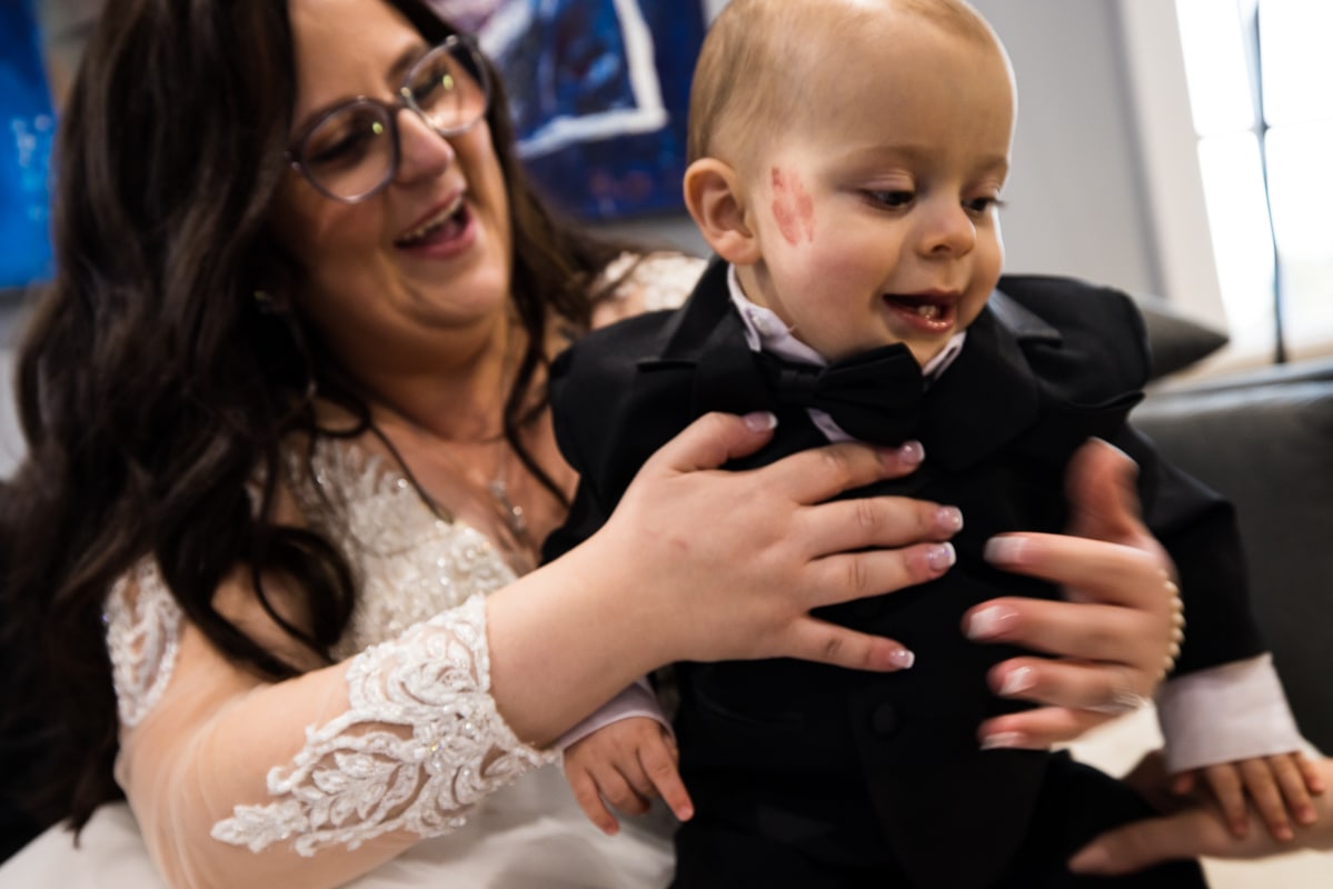 authentic Ryland Inn Wedding Photographer, lisa rhinehart, captures the candid moments of the bride holding a young boy with a lipstick stain on a kiss on his cheek and he smiles down at the floor 