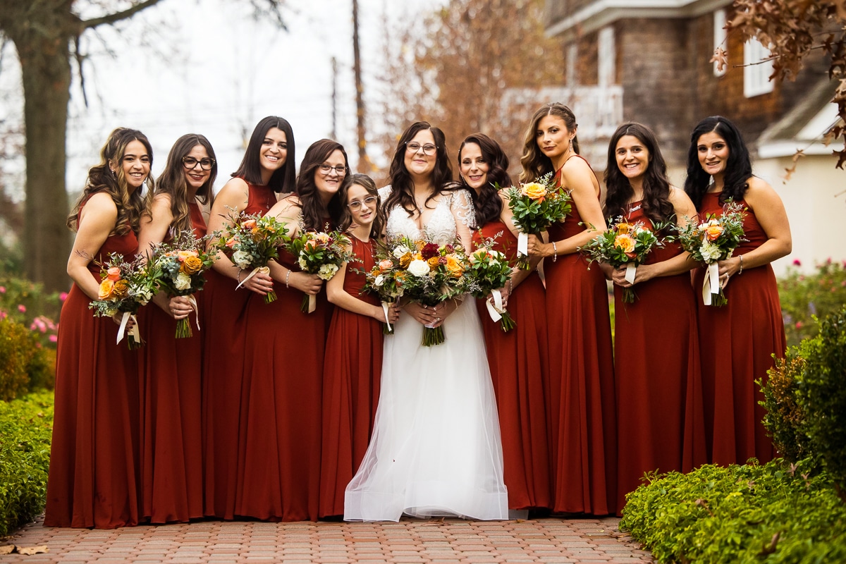 traditional portrait of the bride with her bridal party standing in a straight line in their burnt orange, burgandy dresses and their colorful fall bouquets 