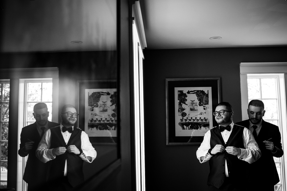 Ryland Inn Wedding Photographer, lisa rhinehart, captured this creative, unique perspective caught in the mirror reflection of the groom buttoning his vest up and a groomsmen helping him get ready before their wedding ceremony at the Ryland Inn 