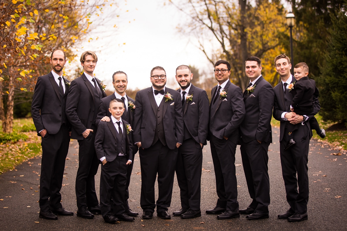 traditional wedding party photo of the groomsmen and the groom standing in a straight line smiling at the camera before the wedding ceremony at the Ryland Inn 