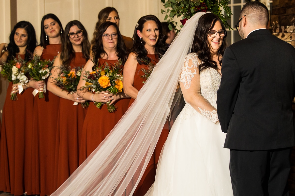 Ryland Inn Wedding Photographer, lisa rhinehart, captures the bride laughing and smiling at the groom as her bridal party stands behind her and smiles at him also 