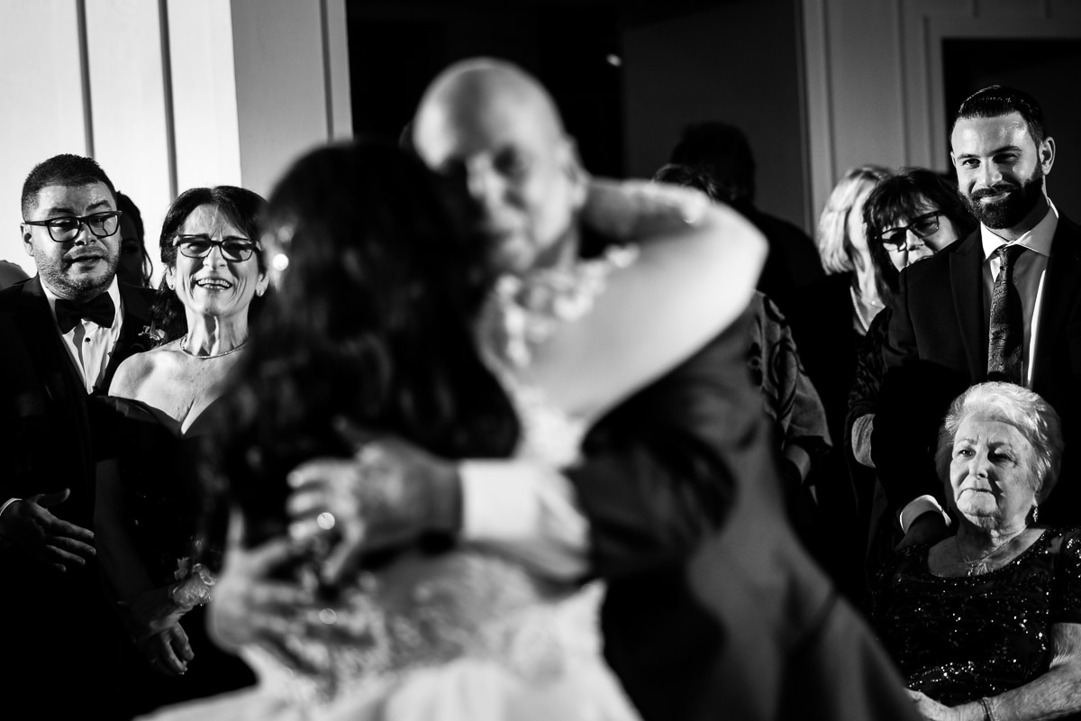 Ryland Inn Wedding Photographer, lisa rhinehart, captures this Black and white image of the bride dancing with her dad which is out of focus and the focus is on everyone else watching her dance and smiling with loving looks as they dance during their ryland inn wedding reception 