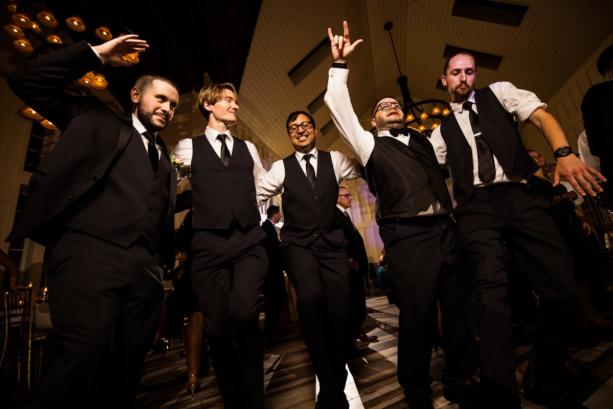image of the groom and his groomsmen dancing together in a line during the wedding reception