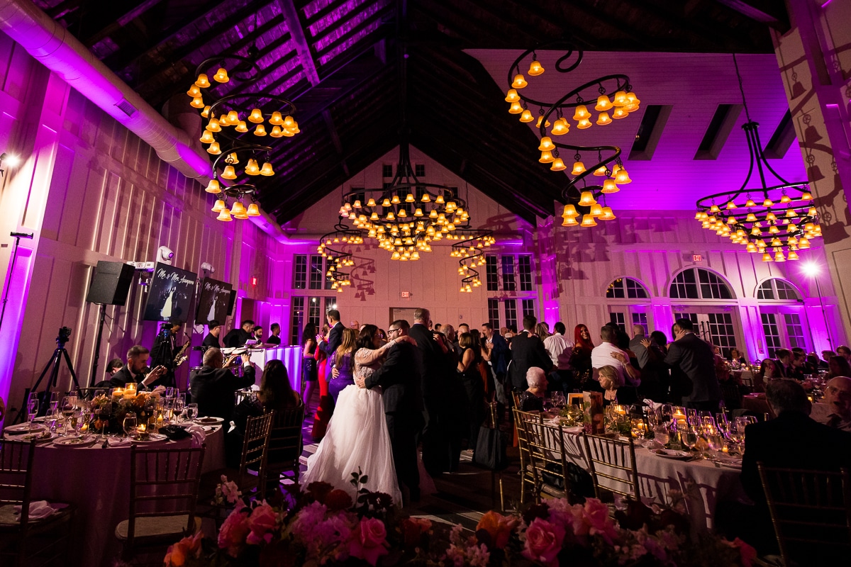 Ryland Inn Wedding Photographer, lisa rhinehart, captures the couple dancing as their guests all dance around them with the room lit up in fushia colored lights and the unique chandeliers of the ryland inn 