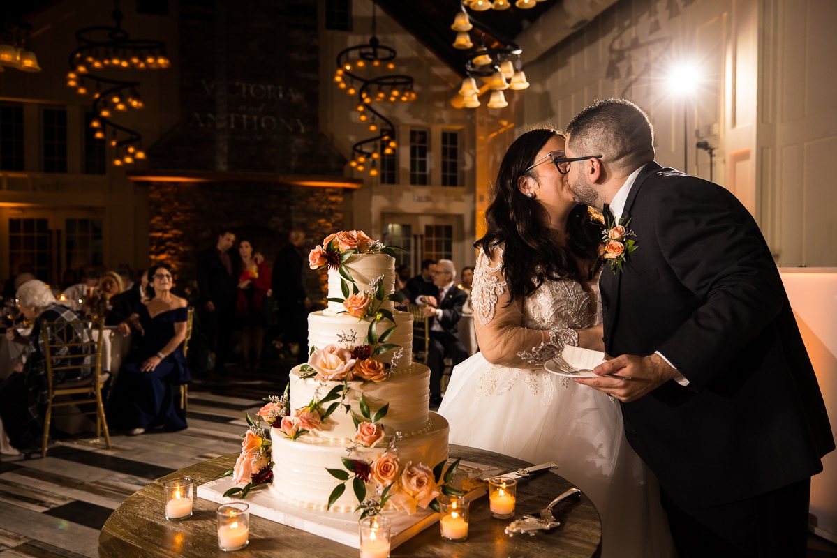 Ryland Inn Wedding Photographer, lisa rhinehart, captures the couple as they kiss when they cut their wedding cake which is a four tiered wedding cake decorated with fall color toned flowers 