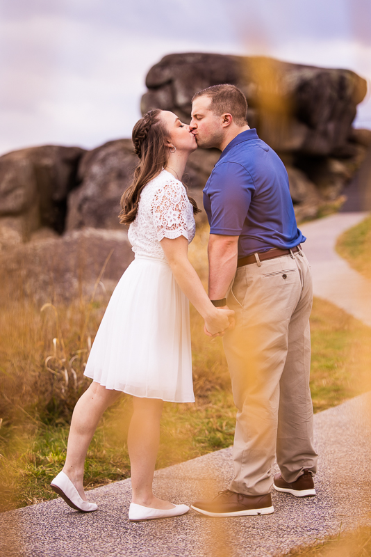 unique, creative image of the couple kissing and holding hands on a pathway with bursts of yellow color from flowers around them during their Devil's Den Gettysburg Engagement