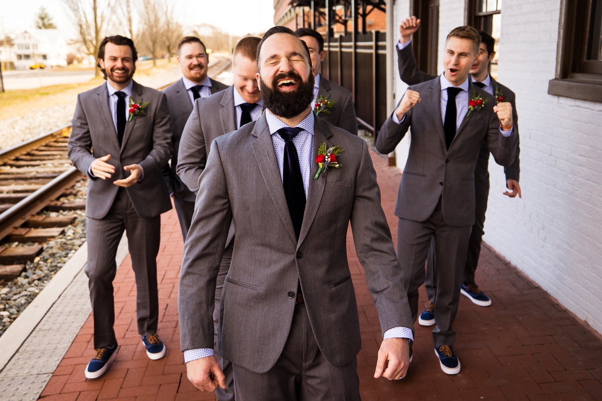 Central PA wedding photographer, lisa rhinehart, captures the groom and his groomsmen laughing and smiling as they walk beside the railroad in downtown Gettysburg before their winter wedding 