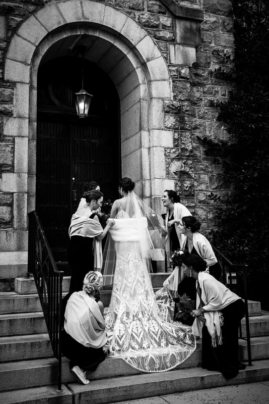 black and white image of the bride getting her dress fixed by her bridesmaids before entering the mount st marys chapel for their wedding ceremony 