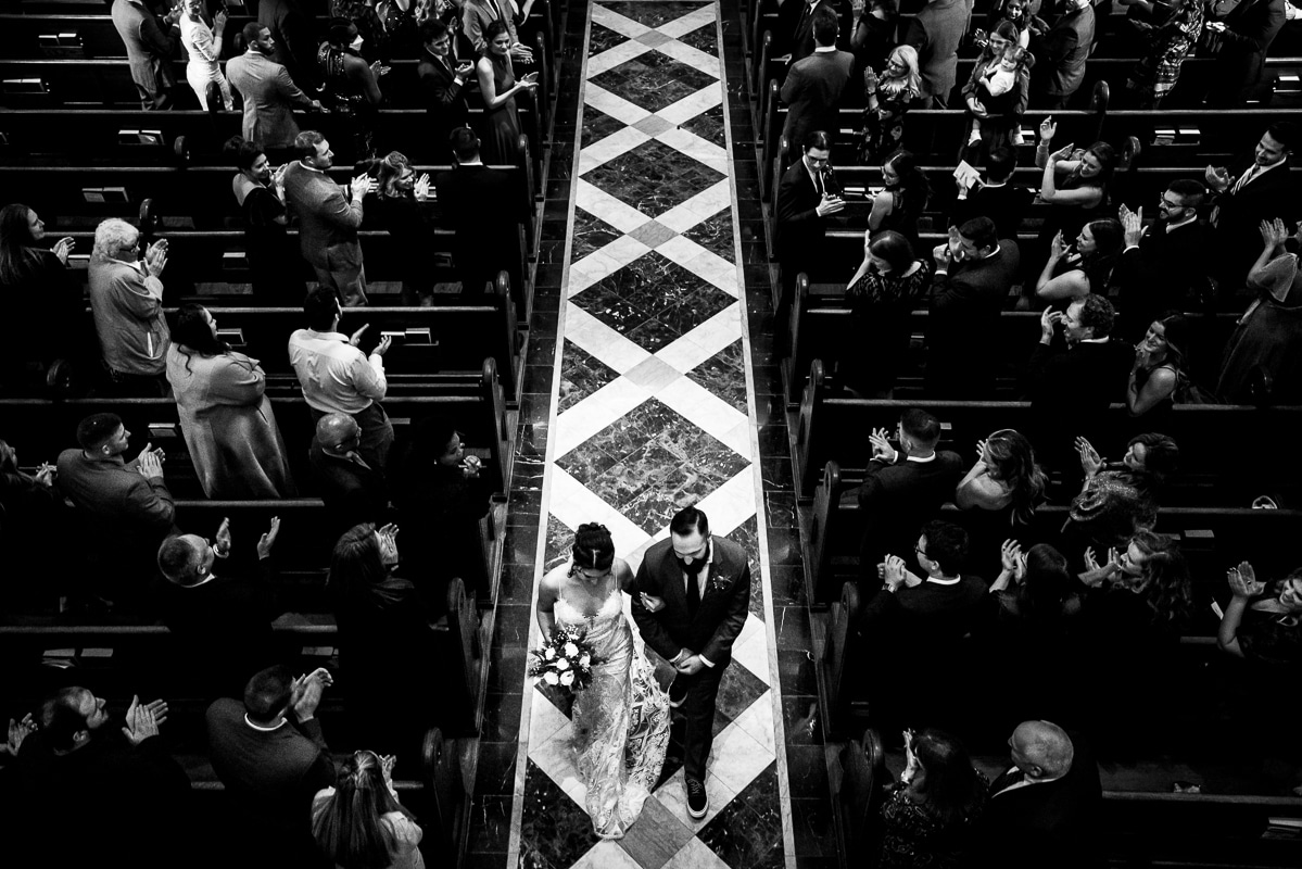 black and white image captures from a unique, creative perspective of the bride and groom as they walk down the aisle at the end of their wedding ceremony at mount st marys chapel