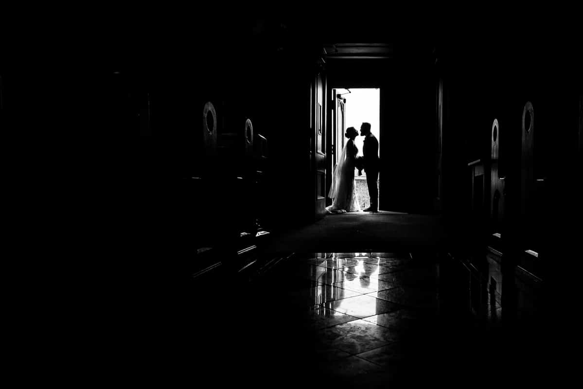 creative, unique black and white image of the bride and groom standing inside of the door way of the chapel at mount st marys captured by Gettysburg Hotel Wedding photographer, rhinehart photography 