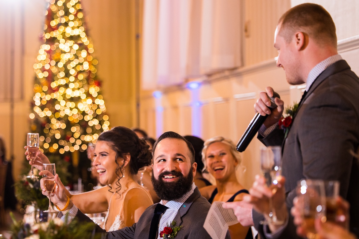 gettysburg wedding photographer, lisa rhinehart, captures the bride and groom laughing and smiling as their friends give speeches and toasts about their relationship during their wedding reception 