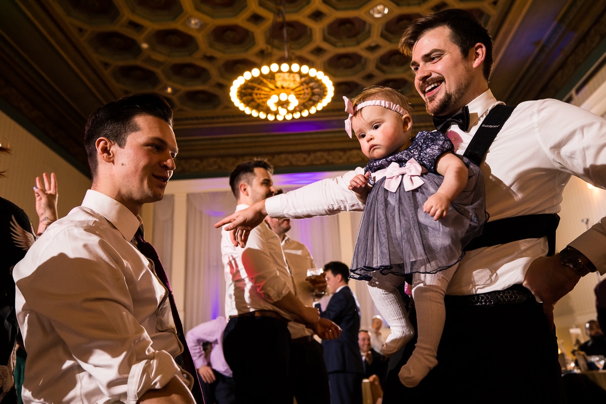 image of groomsmen and guests dancing and singing with a baby during the reception at the hotel 