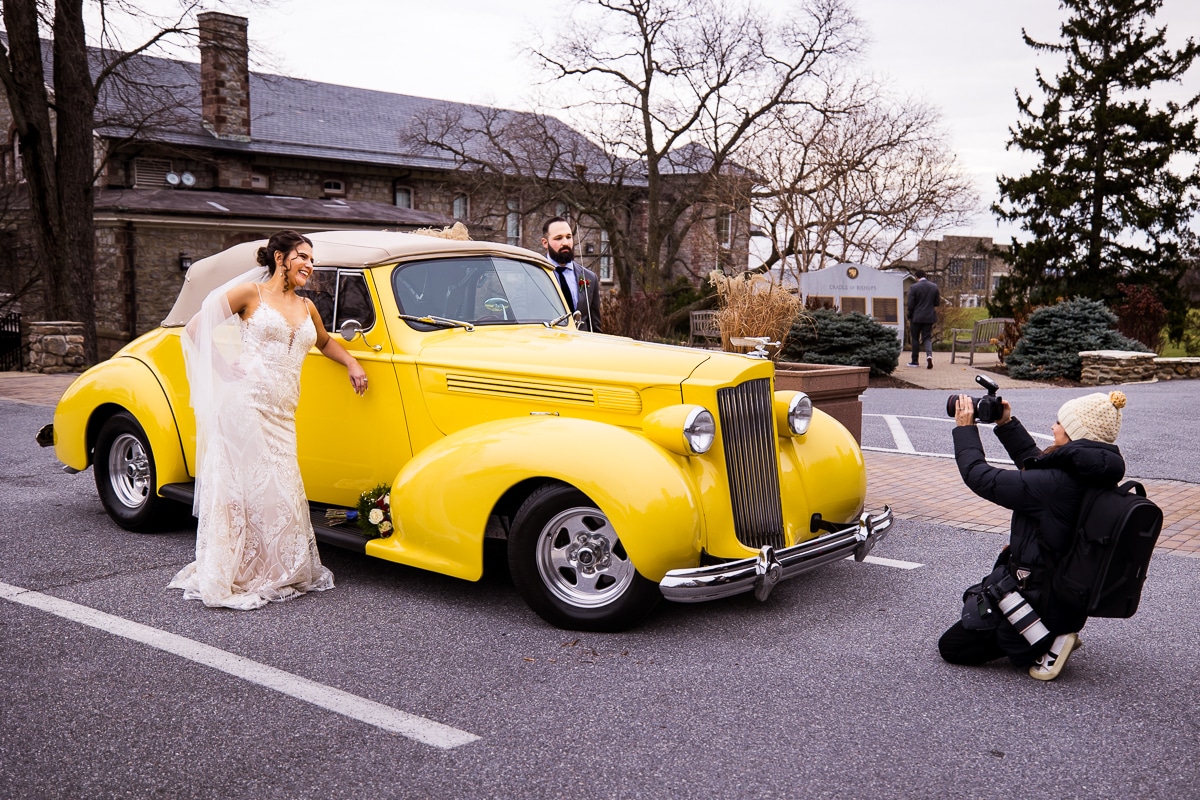 behind the scenes image of rhinehart photography capturing the couple with their grandfathers yellow packard convertible during their mount staint marys wedding 