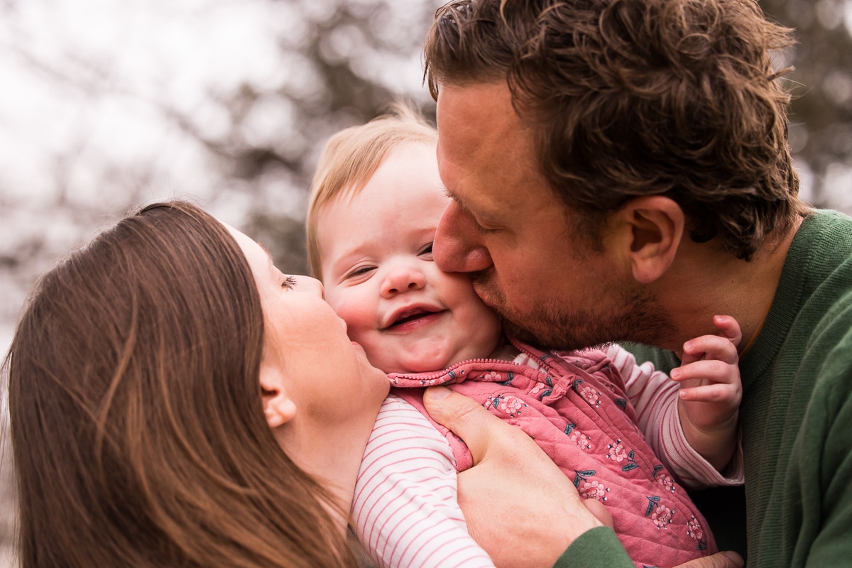 New Cumberland Family photographer, Lisa Rhinehart, captures this image of mom and dad giving lots of kisses to their baby girl outside of their home in pa 