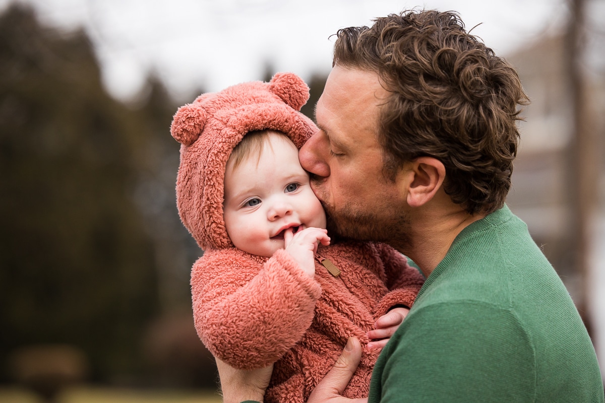 New Cumberland Family photographer, Lisa Rhinehart, captures dad giving kisses to his baby girl in her fuzzy pink bear hoodie in pennsylvania