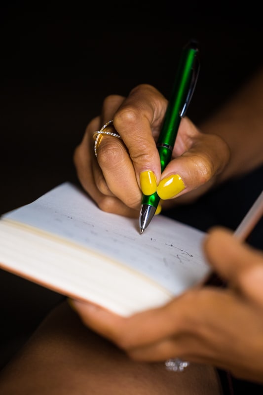 unique image of a woman's hand as she is writing in her journal with a vibrant green pen and bright yellow fingernails 