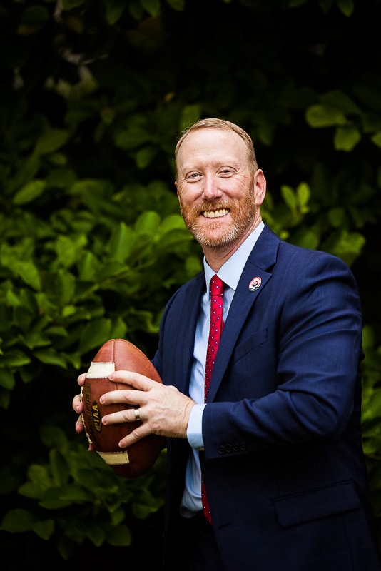 fun, authentic, unique headshot of the university president getting ready to throw a football during his branding photography session 
