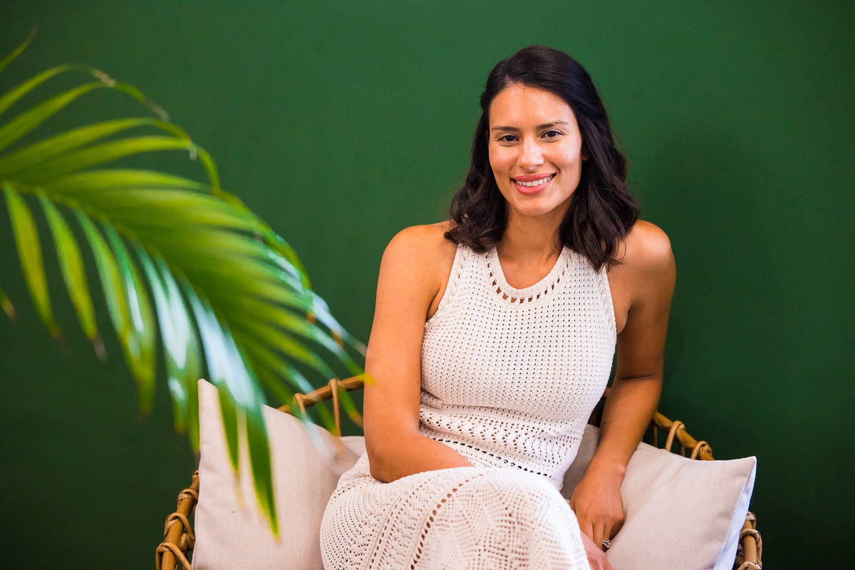 creative branding photographer, lisa rhinehart, captures this vibrant green image of the wall with an out of focus leaf as dermatologist dr. rachel day pops off the image in her white dress as she sits in a chair against the green wall