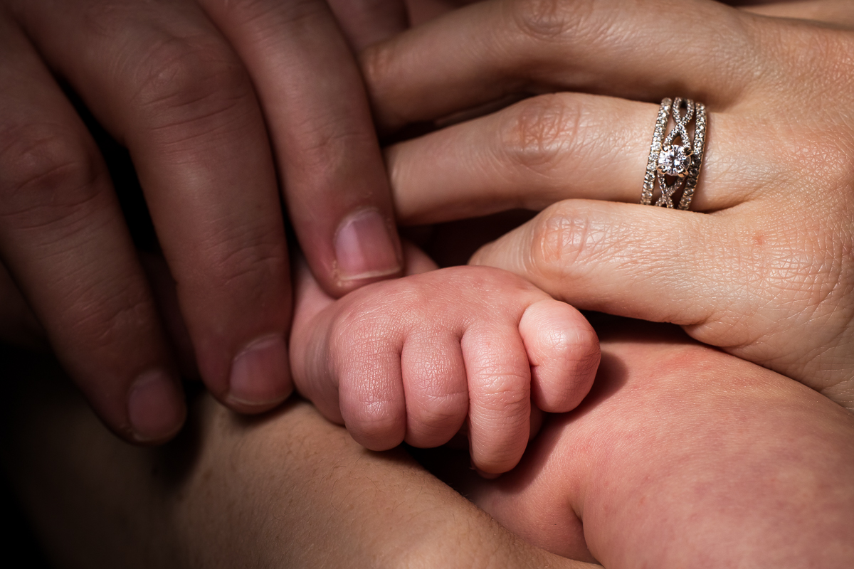 Rhinehart photography captures the newborn baby's hands as his mom and dads hands are wrapped around him during this family session