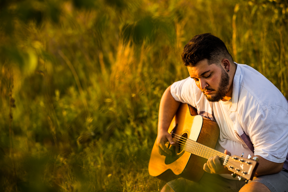 shippensburg senior portrait photographer, lisa rhinehart, captures this authentic, candid image of this graduating senior as he sits in a field and plays some guitar while the sun sets during his senior portrait session 
