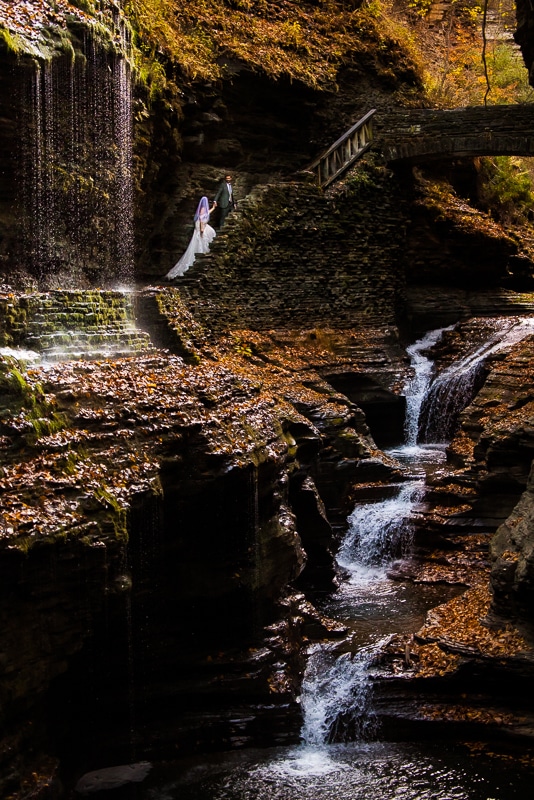 Watkins glen wedding photographer, lisa rhinehart, captures this unique, creative, adventurous shot of this couple in their wedding attire hiking by a waterfall during their after session shoot in New york