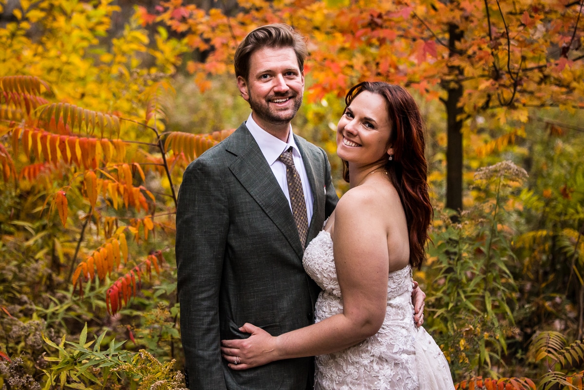 traditional image of the couple standing together hugging as they are surrounded by colorful, vibrant fall leaves while hiking watkins glen state park