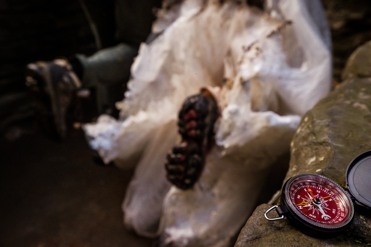 creative, unique, image of the couple hiking in their wedding attire and their hiking boots with mud on their clothes as the camera focuses on a red compass during their after session