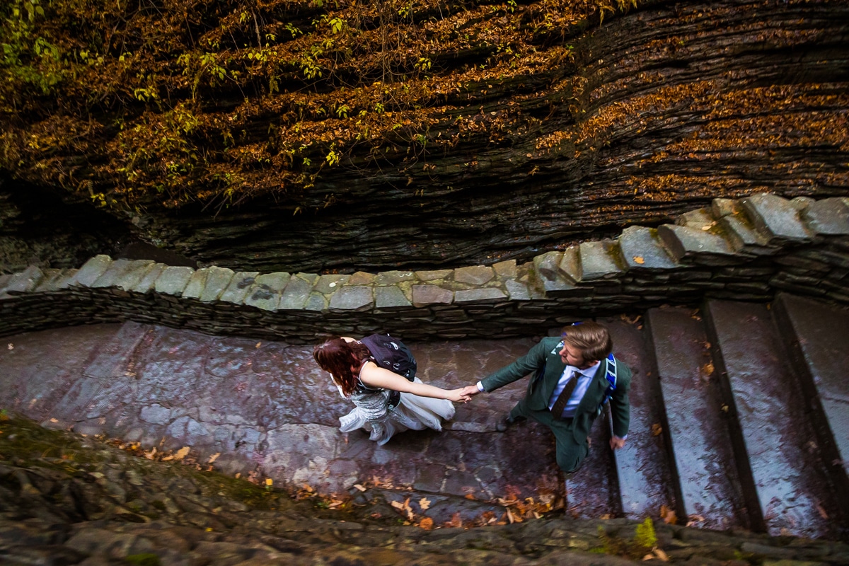 unique, creative perspective and angle of the couple holding hands on the stone made walkway as they explore watkins glen state park during their after session with rhinehart photography 