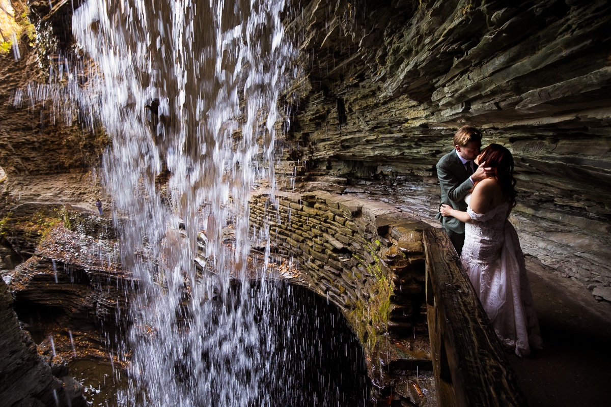 Watkins glen wedding photographer, rhinehart photography, captures this creative, authentic, adventurous image of the couple kissing as the waterfall is beside them during their hike in their wedding attire for their after session