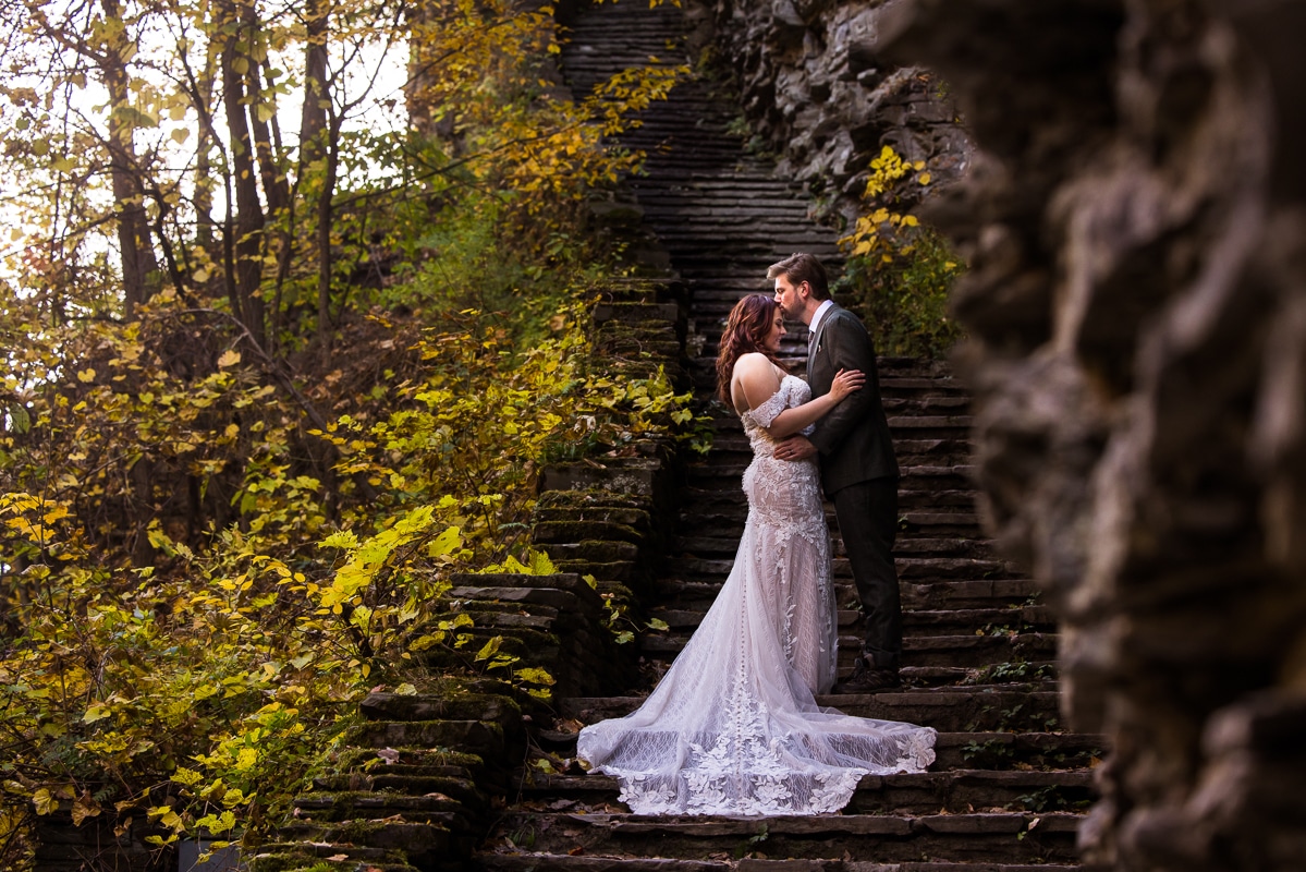 image of the couple in their wedding attire kissing one another on the forehead as they hike through watkins glen during their after session 