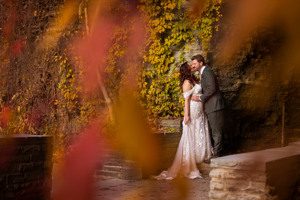 creative, colorful, traditional image of the couple embracing one another as they kiss surrounded by vibrant fall colored leaves as they hike for their after session through watkins glen state park