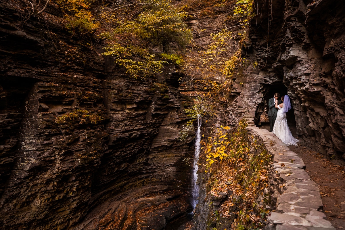 Watkins glen wedding photographer, rhinehart photography, captures this unique, creative, adventurous image of the couple kissing eachothers hands as they are surrounded by rocks, water and nature during their after session hike in their wedding attire 