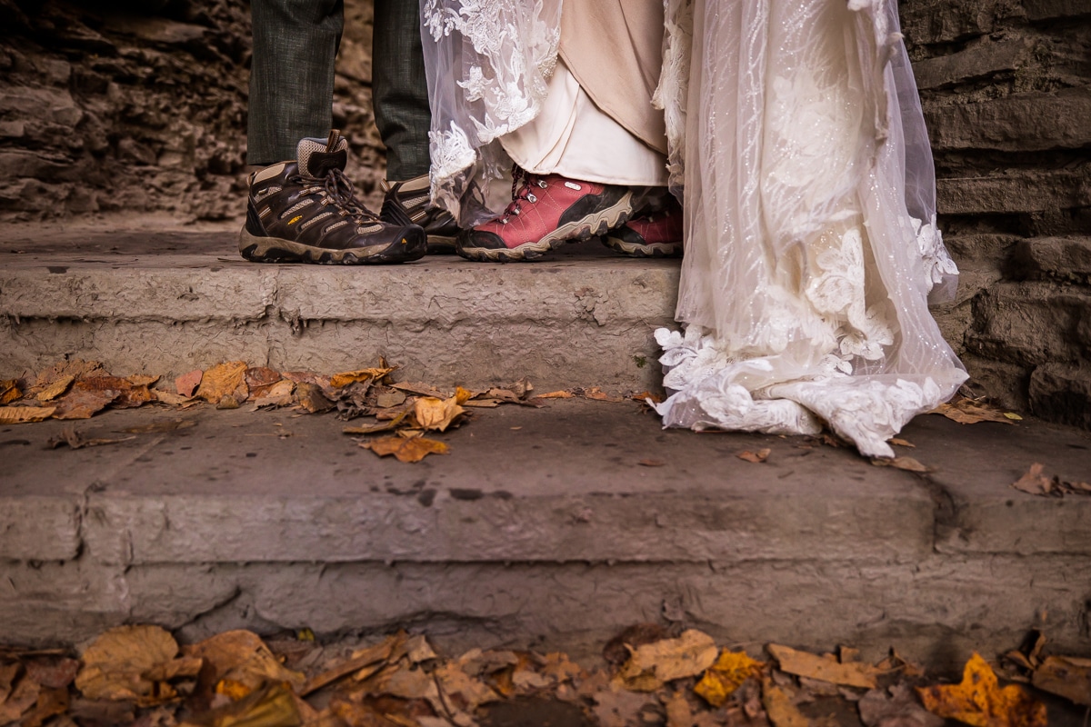 Image of the couple as they stand on the stone stairs in their wedding attire and hiking boots during their after session in a state park in new york 