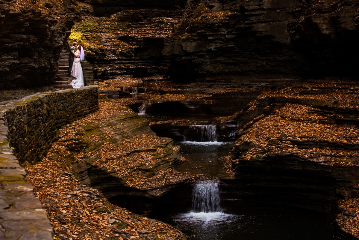 Watkins glen wedding photographer, rhinehart photography, captures this unique image of the couple as they kiss and are surrounded by nature, leaves, rocks and flowing water during their creative, adventurous after session in new york 