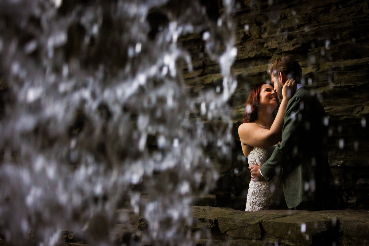 creative after session photographer, rhinehart photography, captures this creative, unique image of the couple as they embrace one another captured through the falling water from the waterfall inside the state park in new york 