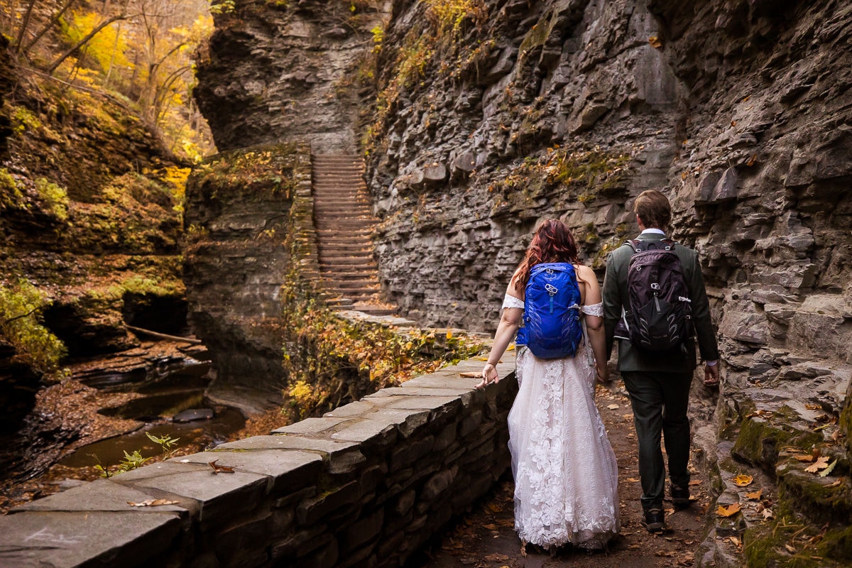 image of the couple as they walk away from the camera with their hiking boots and backpacks on as they get ready to explore watkins glens state park for their after session 