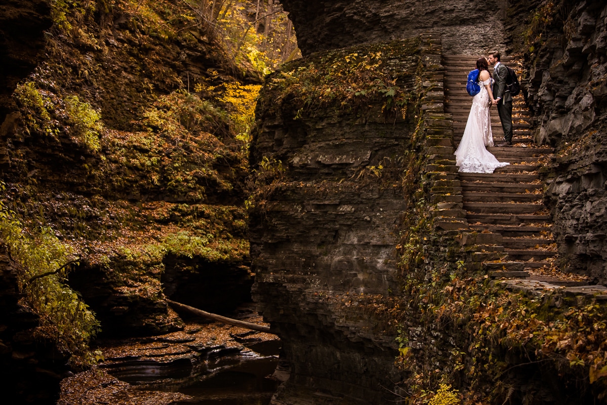 Watkins glen wedding photographer, rhinehart photography, captures this image of the couple kissing one another on the rock staircase surrounded by rocks and water as they explore the state park together during their after session