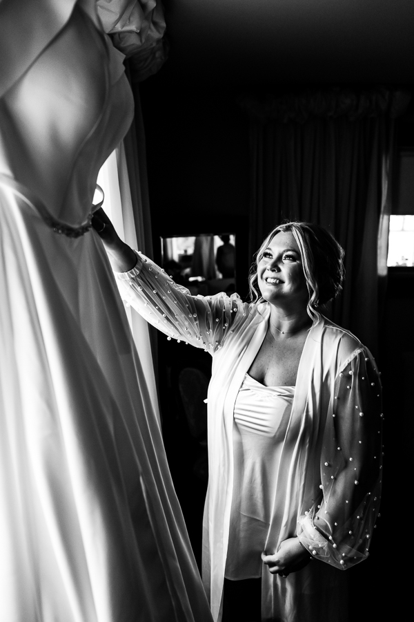 Black and white image of the bride smiling at her wedding dress during her wedding preparations at the barn in virginia
