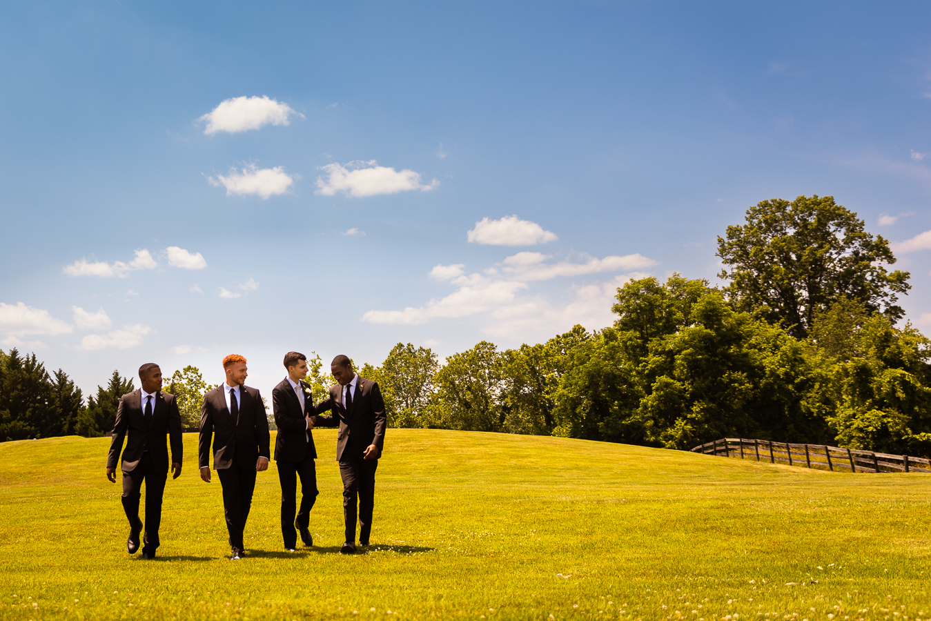 creative, authentic, candid image of the groom as he walks and laughs through the field with his groomsmen captured by virginia wedding photographer, lisa rhinehart