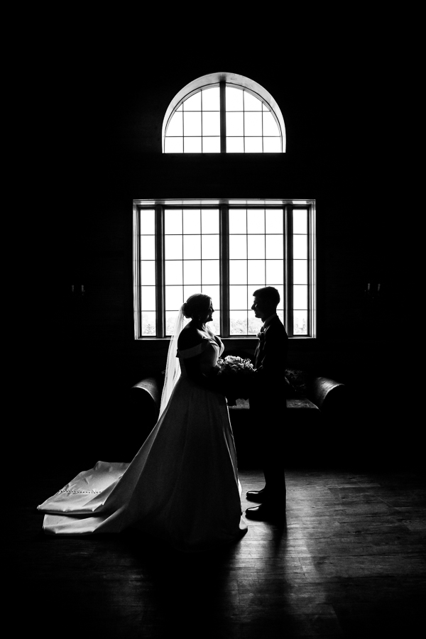 Middleburg Barn Wedding Photographer, lisa rhinehart, captures this black and white dramatically lit image of the bride and groom sharing their first look in front of a giant window before their wedding ceremony 