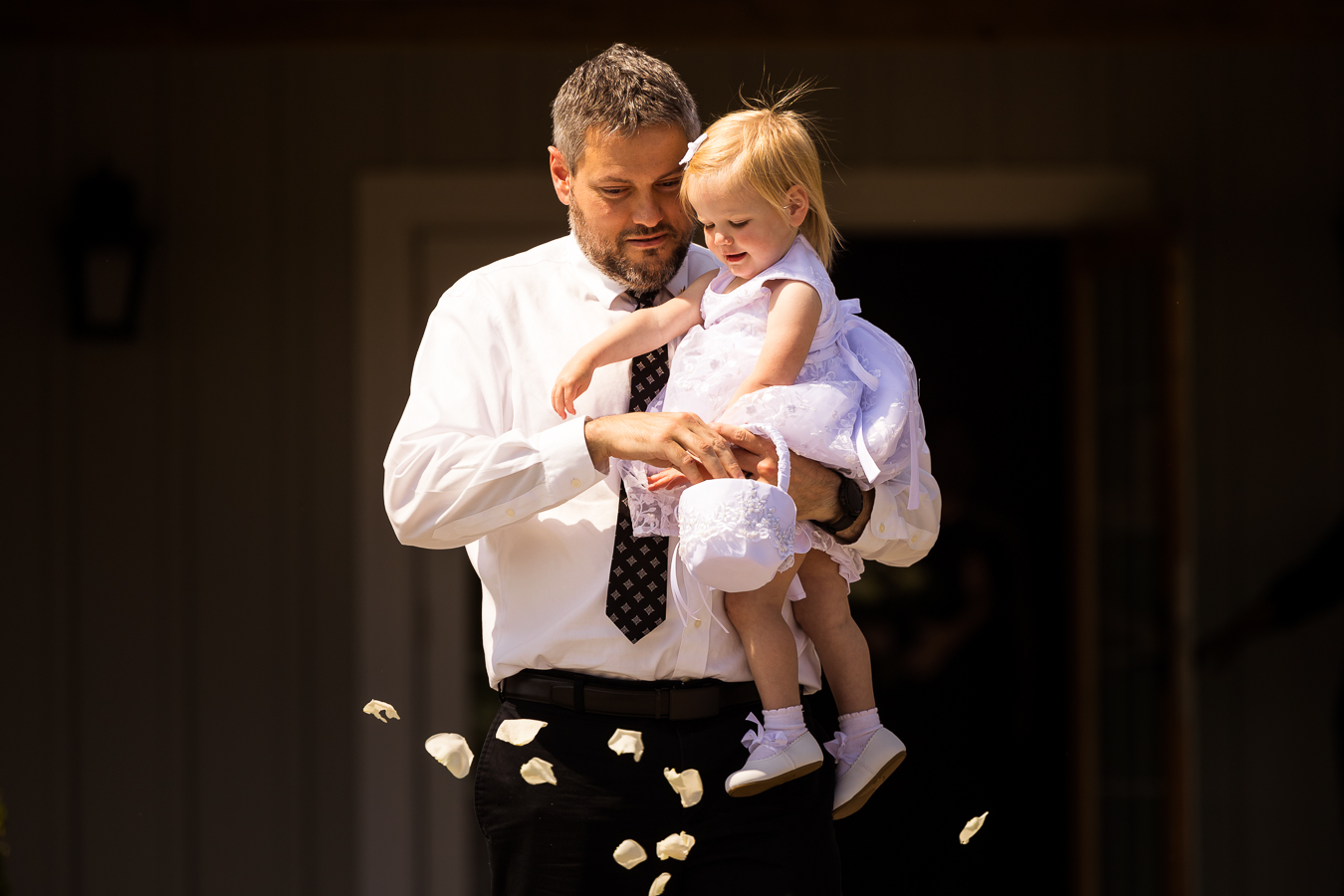 Image of a man holding the baby flower girl and throwing white petals as they walk down the aisle together at the start of the wedding ceremony 