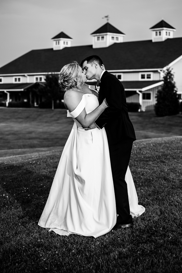 Middleburg Barn Wedding Photographer, lisa rhinehart, captures this black and white image of the bride and groom kissing one another in front of the barn on an open field in Virginia 