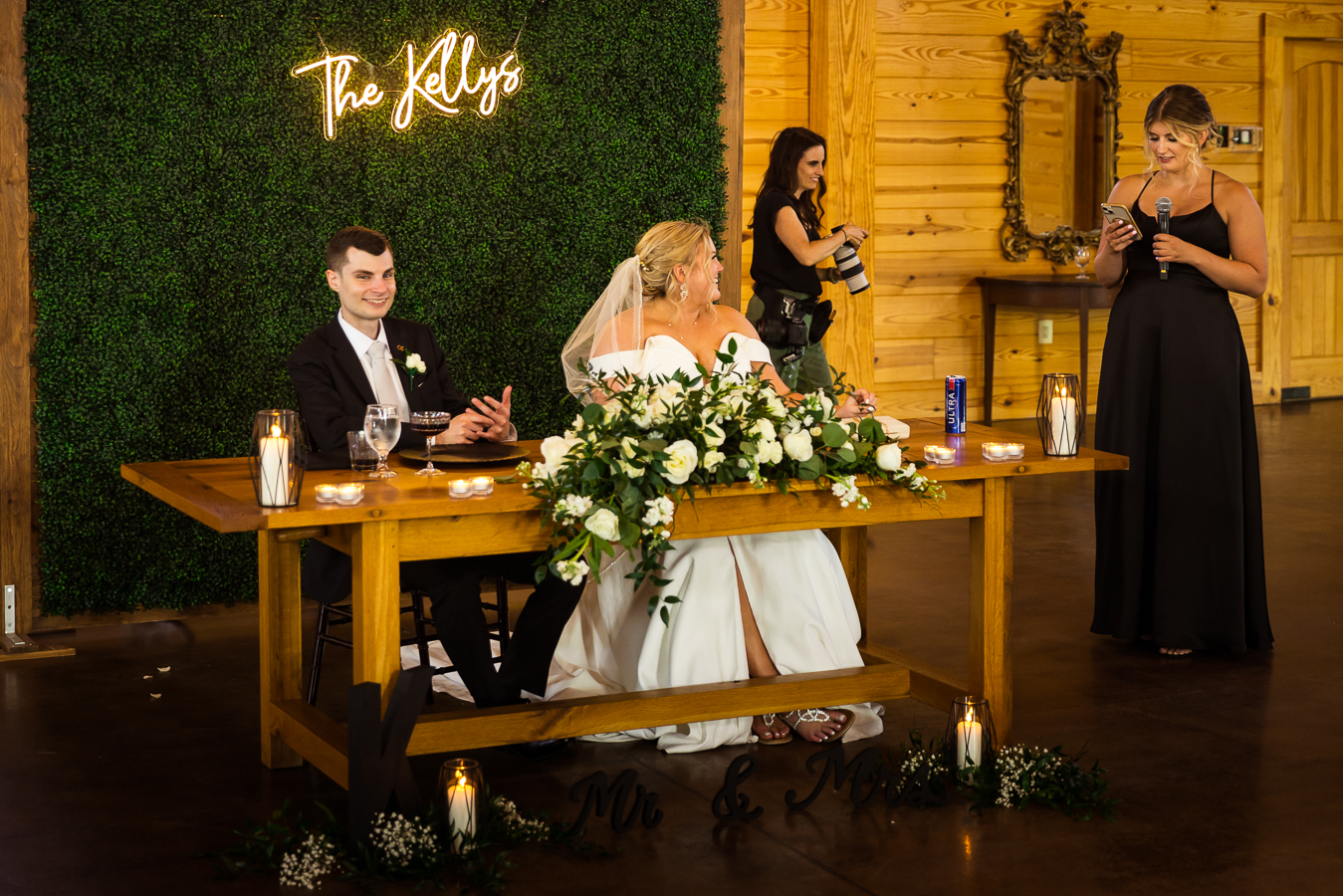 image of the bride and groom sitting at their table while one of the bridesmaids gives a speech during their wedding reception