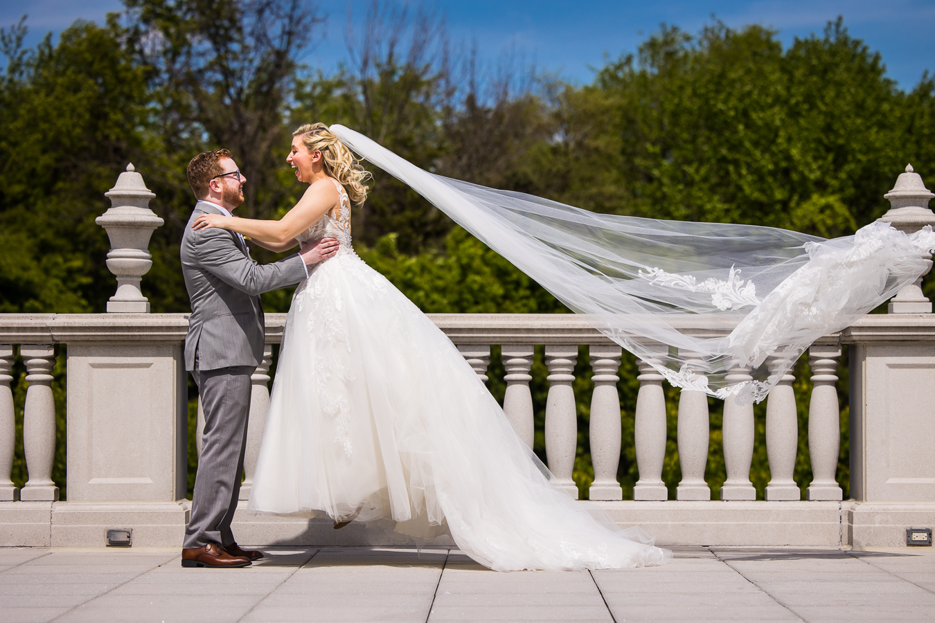 creative NJ Wedding Photographer, captures this candid, authentic moment of the bride jumping with excitement into her groom's arms as her veil blows in the wind behind her during their first look at the palace at somerset park
