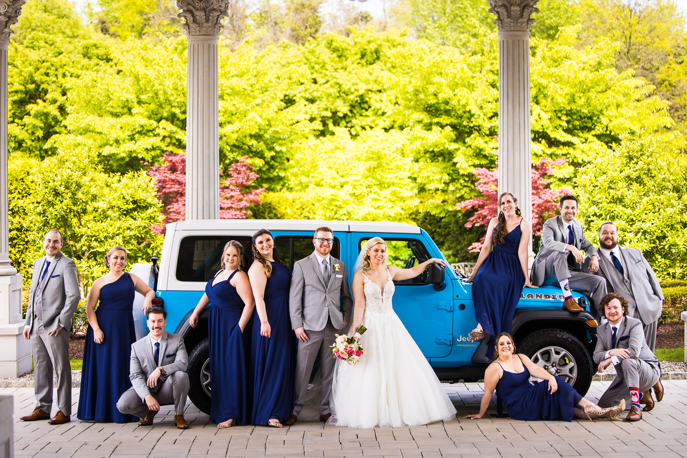 creative NJ Wedding Photographer, lisa rhinehart, captures this fun, creative wedding party image of the bride and groom standing in front of their bright blue jeep as they pose with it
