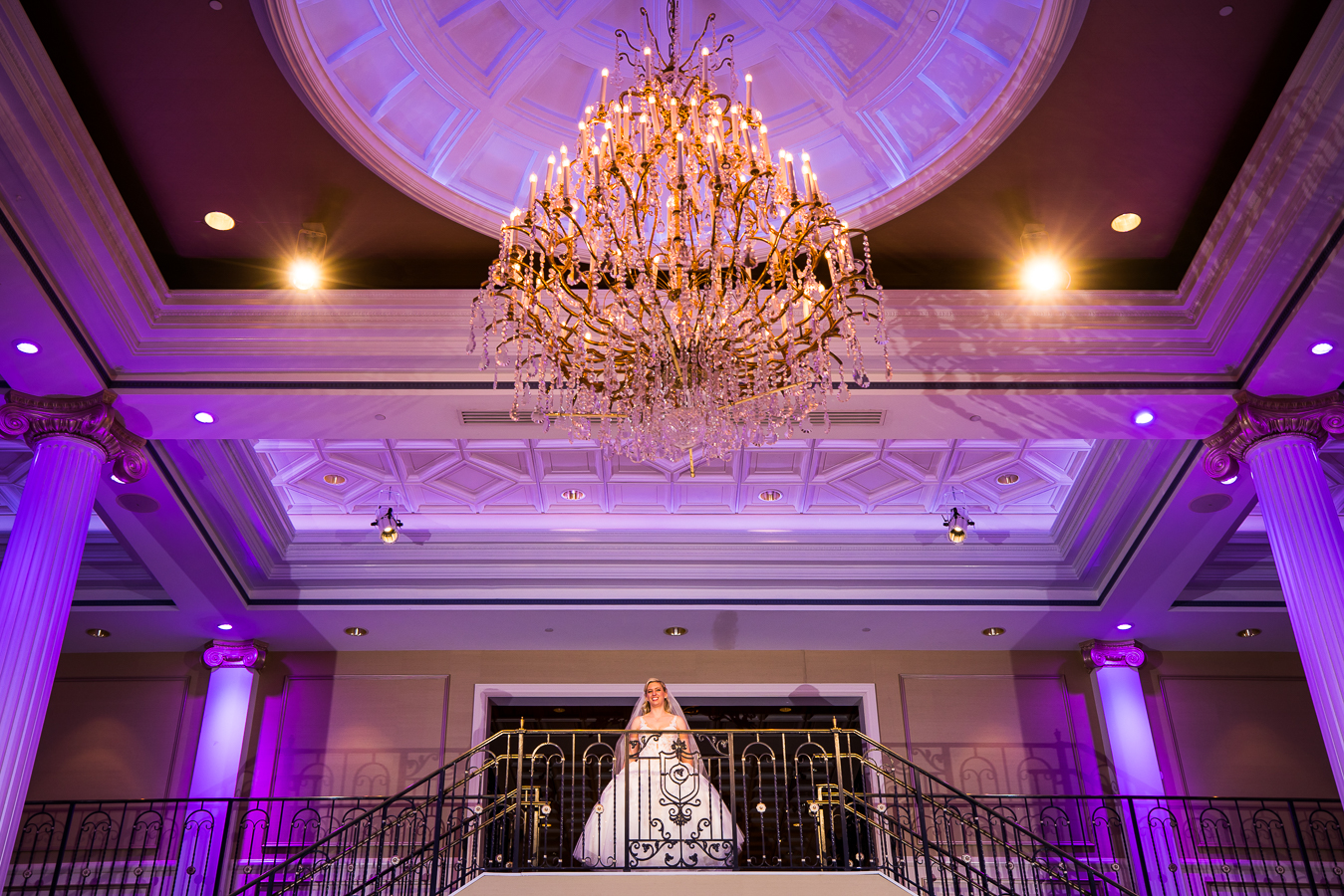 creative NJ Wedding Photographer, lisa rhinehart, captures this stunning, elegant image of the bride as she stands at the top of the grand staircase with a giant chandelier in front of her before walking down to her wedding ceremony at the palace