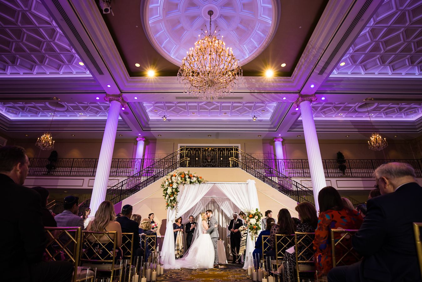 creative NJ Wedding Photographer, rhinehart photography, captures this stunning image of the bride and groom as they kiss one another surrounded by their family and friends inside of the palace at somerset park